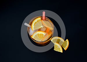 A glass of refreshing lemonade with ice, straws and citrus slices on a black background