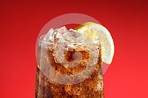 Glass of refreshing soda drink with ice cubes and lemon on red background, closeup