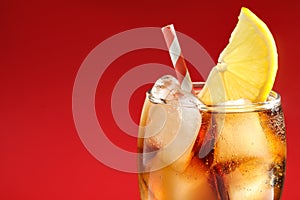 Glass of refreshing soda drink with ice cubes and lemon on red background, closeup. Space for text