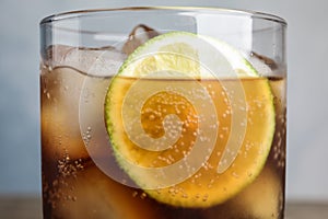 Glass of refreshing soda drink with ice cubes and lime on background, closeup