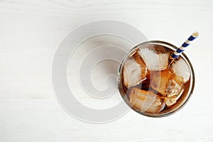 Glass of refreshing soda drink with ice cubes and straw on wooden background, top view. Space for text