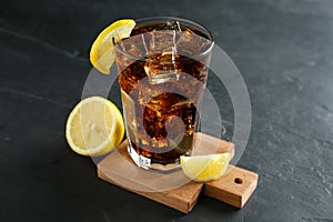 Glass of refreshing soda water with ice cubes and lemon on black table