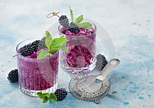 Glass of refreshing summer cocktail with blackberry with ice cubes and mint on light blue background with strainer