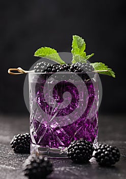 Glass of refreshing summer cocktail with blackberry, ice and mint on black background with raw berries