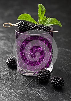 Glass of refreshing summer cocktail with blackberry, ice and mint on black background with raw berries