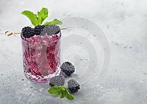 Glass of refreshing summer cocktail with blackberry, ice and mint on light background. Soda and alcohol mix