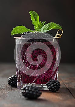 Glass of refreshing summer cocktail with blackberry, ice and mint on wooden background with raw berries