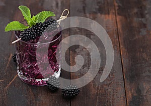 Glass of refreshing summer cocktail with blackberry, ice and mint on wooden background. Soda and alcohol mix