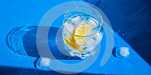 A glass of refreshing water with ice and lemon on a blue background. Heat concept, fresh. Natural light. Flat lay, top view, copy