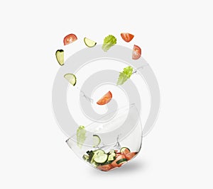 Glass salad bowl in flight with vegetables: tomato, cucumber and leaf salad. Isolated on white background. healthy diet
