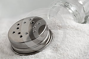 Glass salt shaker and metal lid lying on top of sea salt