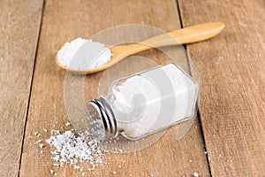 Glass salt shaker on wooden and salt on wooden spoon