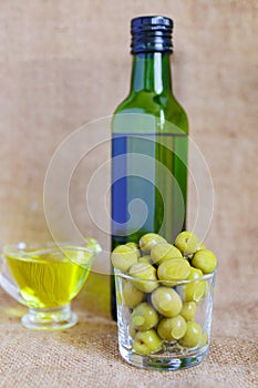 Glass sauceboat with extra virgin olive oil.  fresh green olives and bottle on wooden table