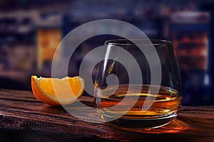 Glass of scotch whiskey and orange slice wood rustic table dark bar background