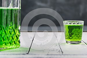 Glass shot and bottle of absinthe in carafe on table of bar. Alcohol consumption in restaurant, alcoholism in urban society