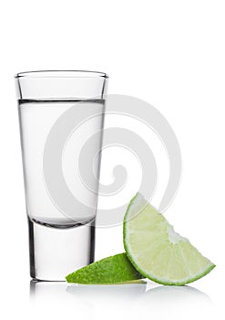 Glass shot of silver tequila with lime slices on white photo