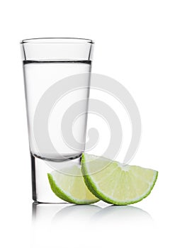 Glass shot of silver tequila with lime slices on white photo