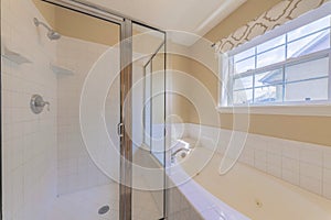 Glass shower stall and bathtub with white tiles surround