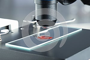 Glass slide with sample of red liquid under microscope in laboratory, closeup