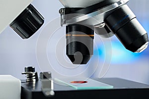 Glass slide with sample of red liquid under microscope in laboratory, closeup