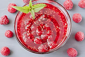 Glass small saucer with raspberry jam with fresh raspberries and mint close-up on gray background