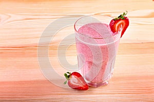 Glass of smoothie with ripe and fresh strawberries and organic milk on a light brown wooden table. Milkshake with strawberries.