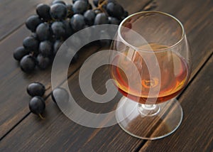 A glass snifter of brandy or cognac with a bunch of black grapes