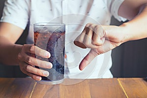 Glass of softdrink splashing with ice on hand wooden table background, not good bad for health finger symbol