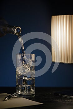 A glass of sparkling water with ice on a dark table with a pen and a sheet of paper.