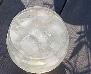 A glass of sparkling water and ice on a gray wooden background. Top view