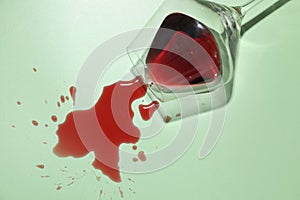 Glass with spilled red wine on light green background, top view
