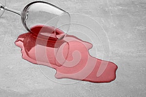 Glass with spilled red wine on light grey surface, closeup