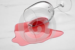 Glass with spilled red wine on white marble surface, closeup