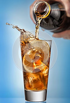 Glass of splashing iced tea with lemon on blue background