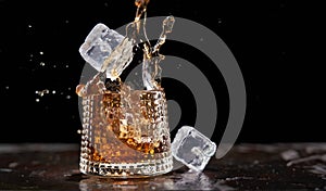 Glass of splashing whiskey with icecube on stone table, on black background