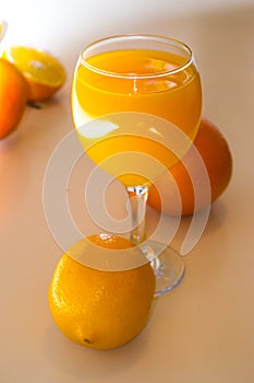 A glass of squeezed orange juice closeup, fresh and juicy oranges and lemon on a bright yellow and white background..