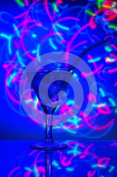 Glass with a straw cocktail with ice against a backdrop of abstract illumination