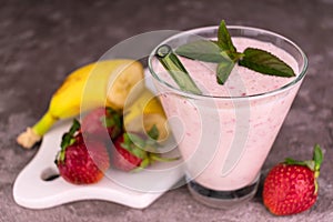 A glass of strawberry banana milkshake on a gray background.