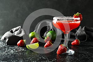 Glass of strawberry daiquiri cocktail, limes and berries on dark background