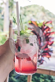 Glass of strawberry juice with soda in man hand. Tropical cafe background. Bali island.