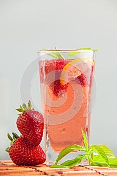 Glass of strawberry lemonade with pieces of strawberry, lemon and fresh mint.