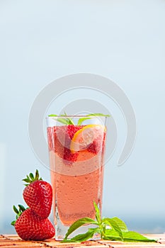 Glass of strawberry lemonade with pieces of strawberry, lemon and fresh mint.