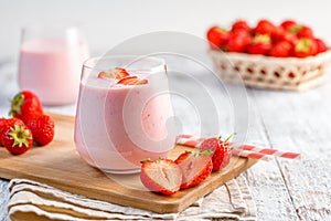 Glass with strawberry smoothie or milkshake on wooden table.