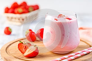 Glass with strawberry smoothie or milkshake on wooden table.