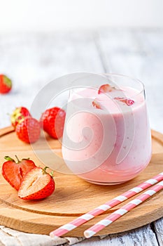 Glass with strawberry smoothie or milkshake on wooden table.