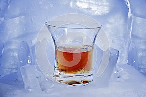 Glass with a strong alcoholic drink of whiskey color stands on the broken blue ice.