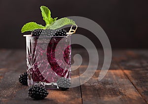 Glass of summer cocktail with blackberry with ice cubes and mint on wooden background with berries. Soda and alcohol mix