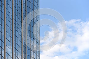 Glass surface of a building with reflection and blue sky with a cloud
