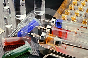 Syringes with medication on sterilization box, ampoules and vials with fluid on glossy surface. Toned