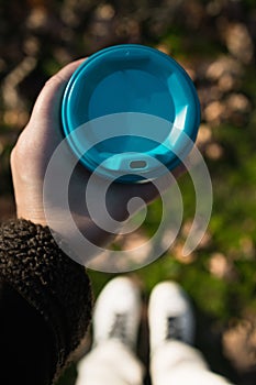 a glass with takeaway coffee in hands, against the background of blurry autumn leaves, top view